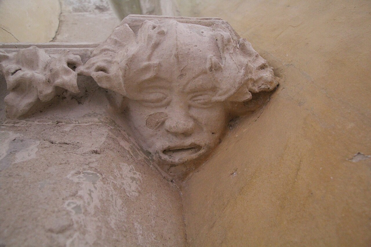 Chip de Om Verde sculptat în piatră, cu frunze în jurul feței, în biserica din Richiș